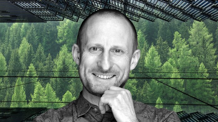 Smiling Prof. Jakub Kronenberg on the background of green trees. In the picture there are also glass facades of skyscrapers.