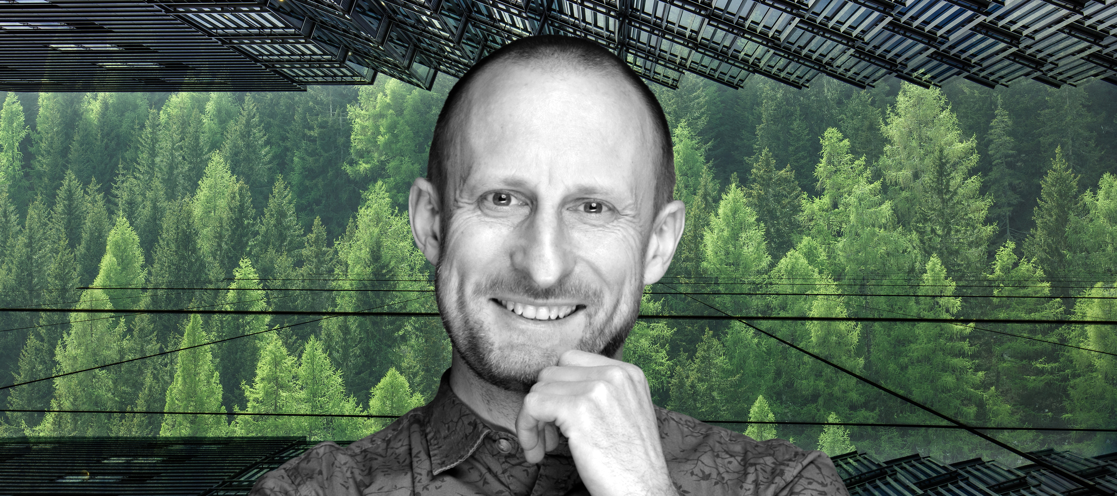 Smiling Prof. Jakub Kronenberg on the background of green trees. In the picture there are also glass facades of skyscrapers.